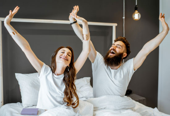 Man and woman in bed stretching after soaking in their hot tub and getting a good nights rest