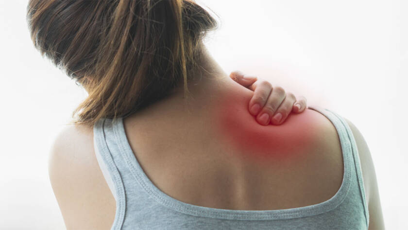 Woman’s back with red spot to signify muscle pain, her hand on her shoulder.