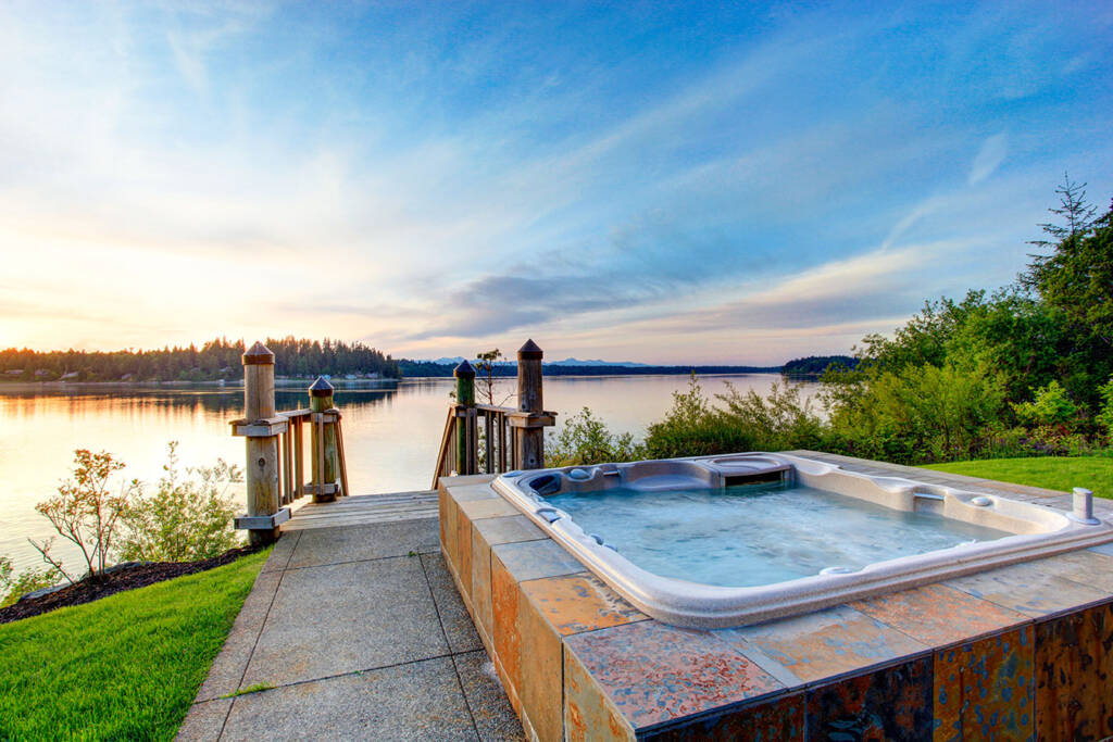 Hot tub in the summer by a lake in a backyard with the sun beaming over the horizon