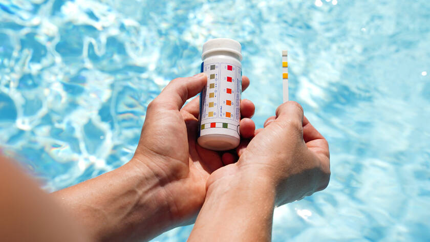 Person holding pH test strips test strips over hot tub water