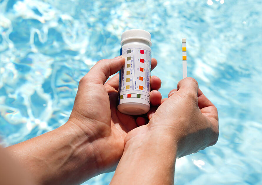 Person holding pH test strips test strips over hot tub water